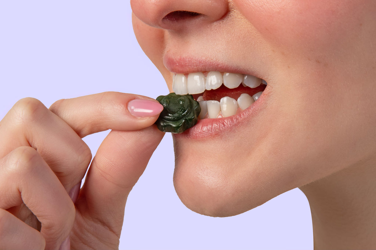 Mulher mordendo uma gummy de Suco Verde Guday sobre fundo lilás